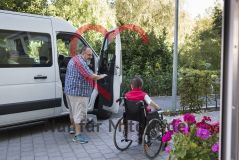 Ein Mann steht neben einem Auto und spricht mit einer alten Frau Seniorin im Rollstuhl