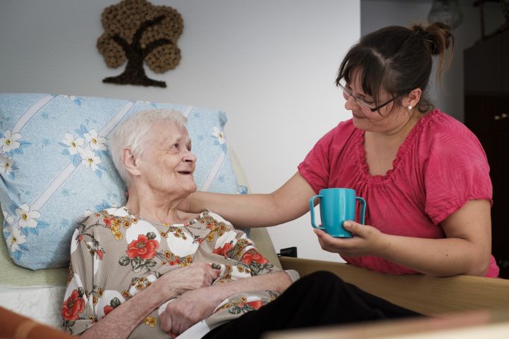 Pflegerin reicht Seniorin Tee