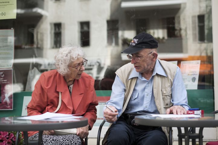Eine Seniorin und ein Senior sitzen in einem Straßencafe und reden miteinander