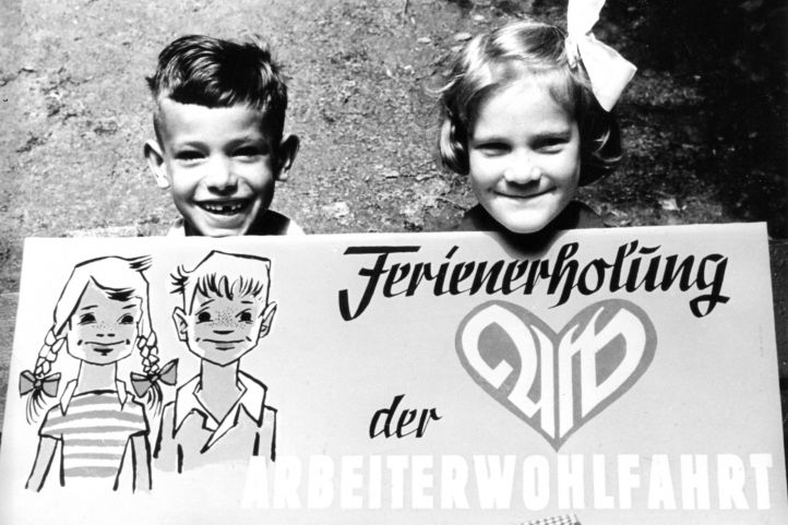 Ferienfreizeit der AWO historisches BIld mit lachenden Kindern einem Jungen und einem Mädchen und einem Plakat Ferienerholung