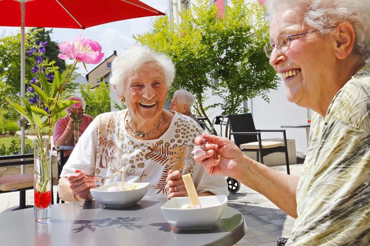 Zwei ältere Frauen sitzen am Tisch und essen mit Löffeln Eis aus der Schale