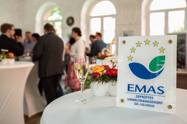 Emas-Schild auf einem Tisch mit Menschen im Hintergrund bei der Zertifizierung