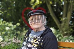 Ein alter Mann Senior sitzt drauen auf einer Bank und lächelt in die Kamera