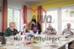 Mehrere alte Menschen Seniorinnen und Senioren sitzen am Tisch und essen und eine Frau hilft ihnen